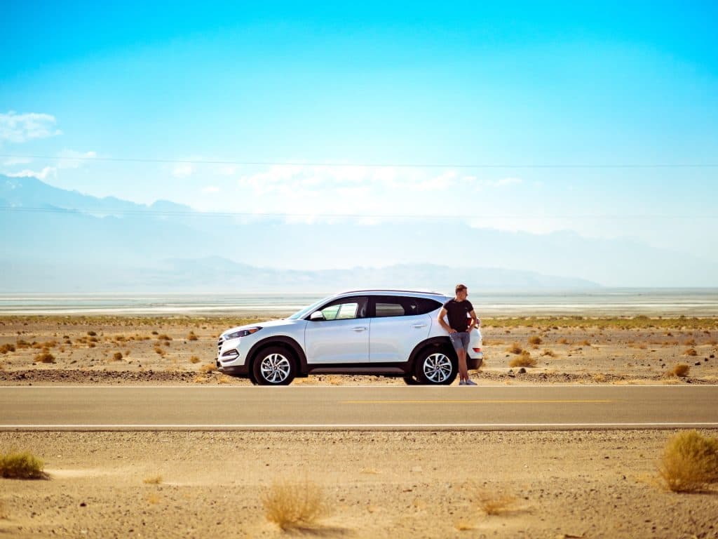 Hombre apoyado en el coche, que está en un desierto